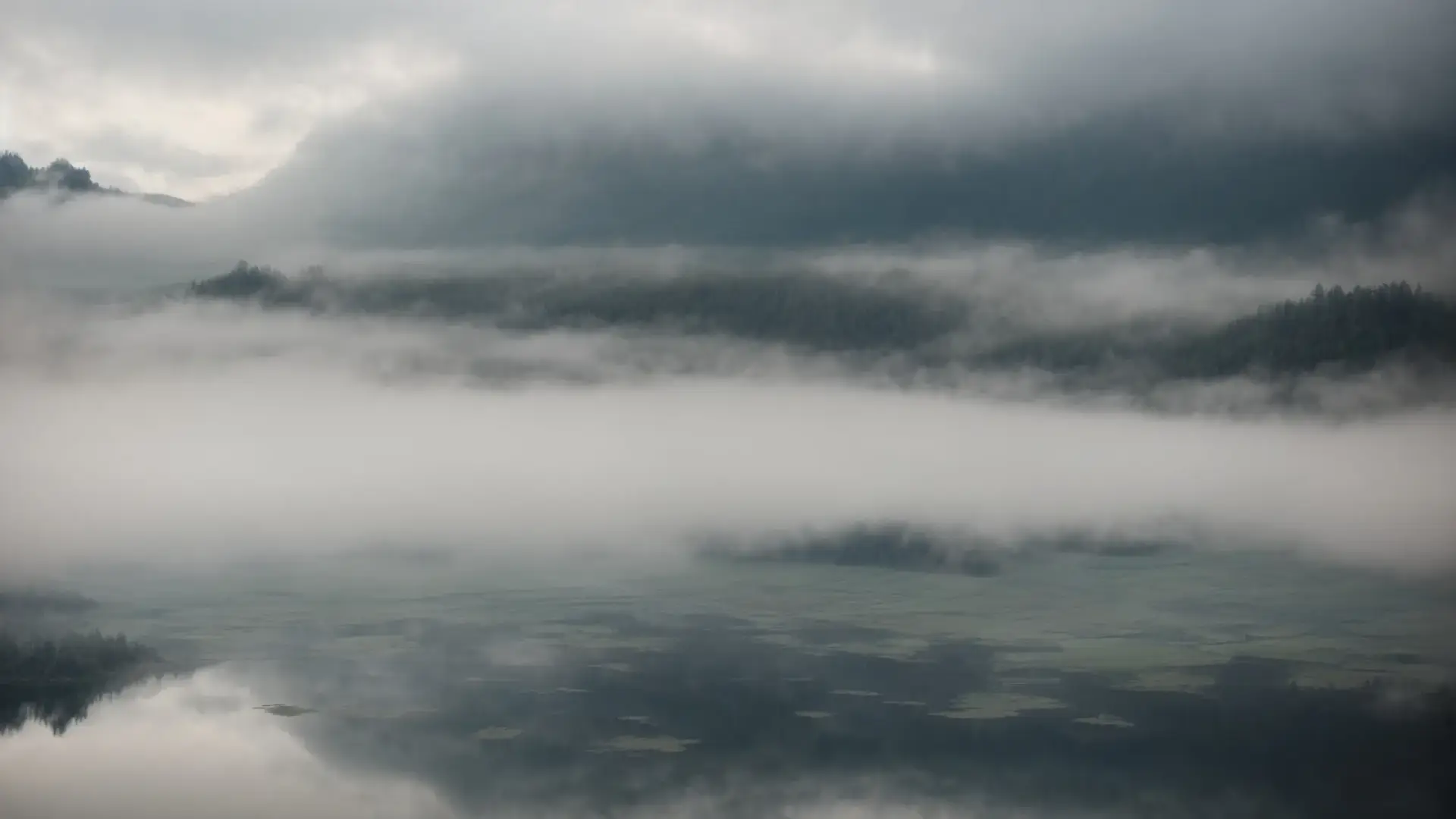 a cloudy sky reflecting in a still lake, surrounded by fog.